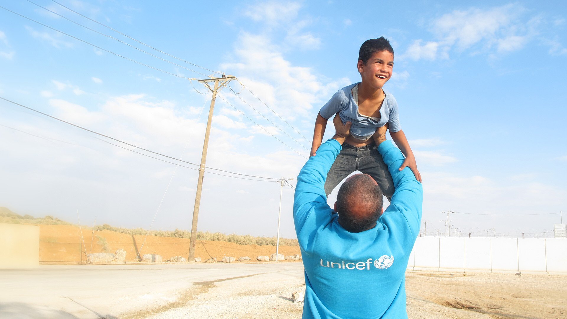 Ein Junge wird von UNICEF Mitarbeiter in die Höhe gehalten.