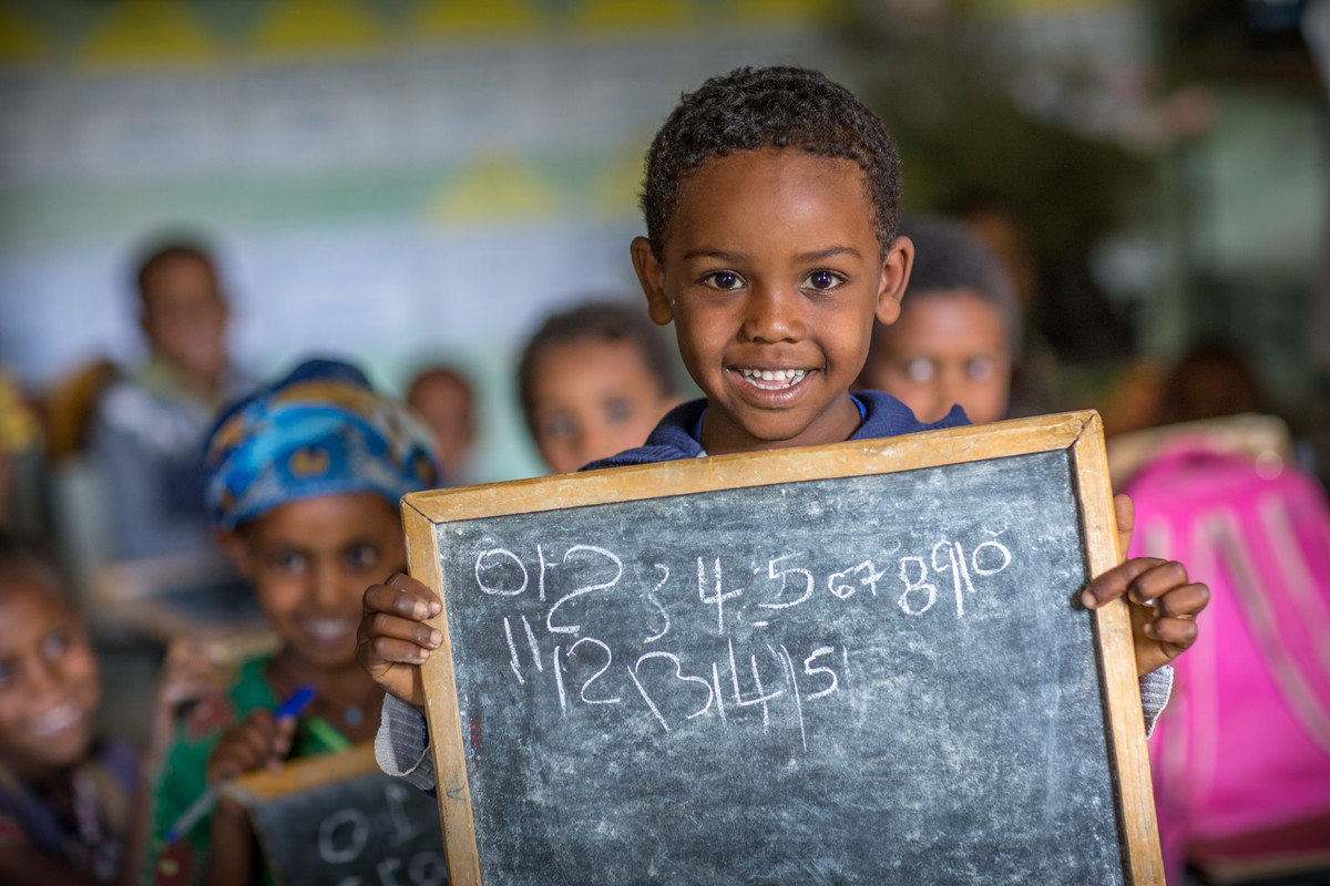 Kind in der Schule, welches eine vollgeschriebene Tafel in der Hand hält.