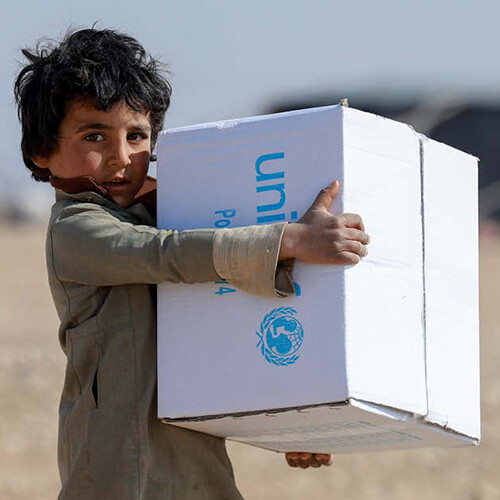Junge mit UNICEF-Hilfsgüterkiste auf dem Arm.