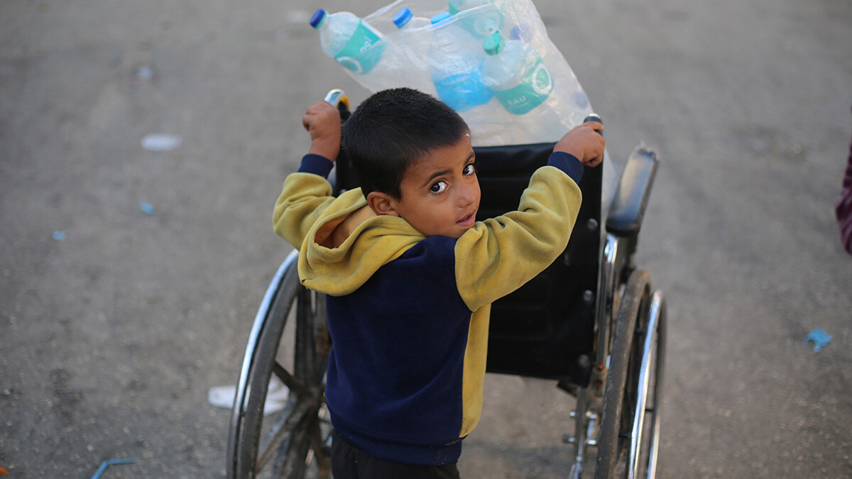 Ein Junge schiebt einen Rollstuhl mit leeren Wasserflschen beladen durch die Strassen Gazas.