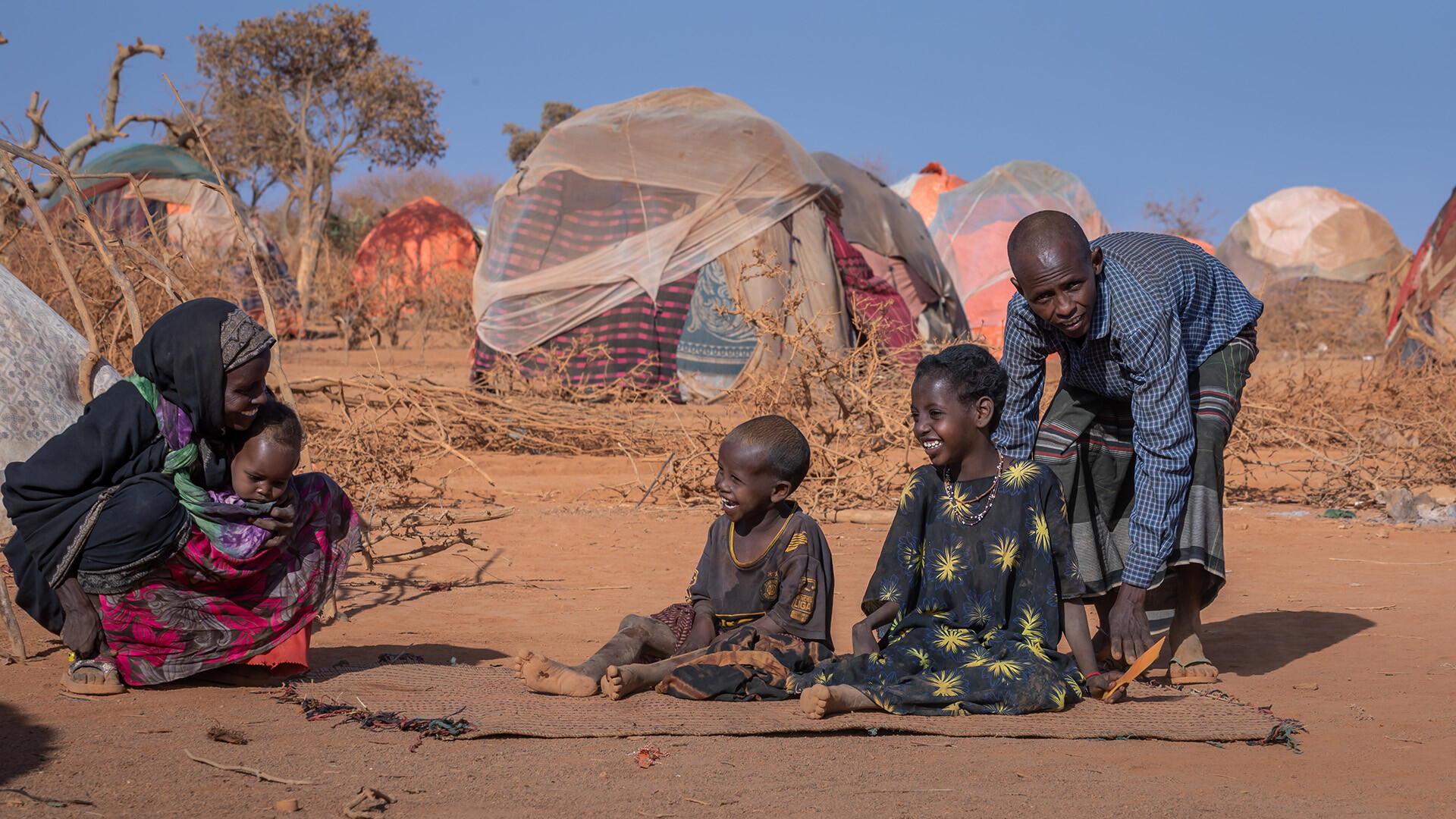 Eine junge Familie sitzt in Äthiopien in einem Notlager und lacht.