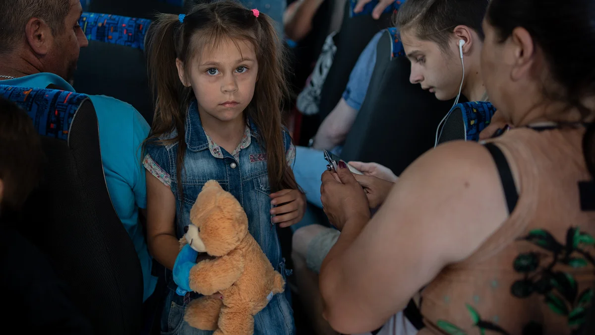 Dmytro, ein Vater von fünf Kindern (links mit dem Rücken), seine Tochter Anya, 7 Jahre alt, und sein Sohn Ernest, 15 Jahre alt (rechts, mit Kopfhörern) sitzen im Evakuierungsbus am Busbahnhof von Cherson.