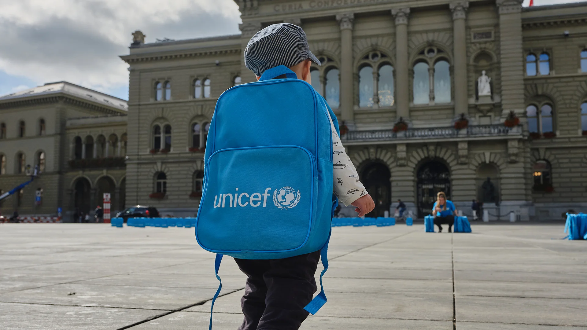Ein kleiner Junge läuft mit UNICEF Rucksack auf dem Platz vor dem Bundeshaus in Bern.