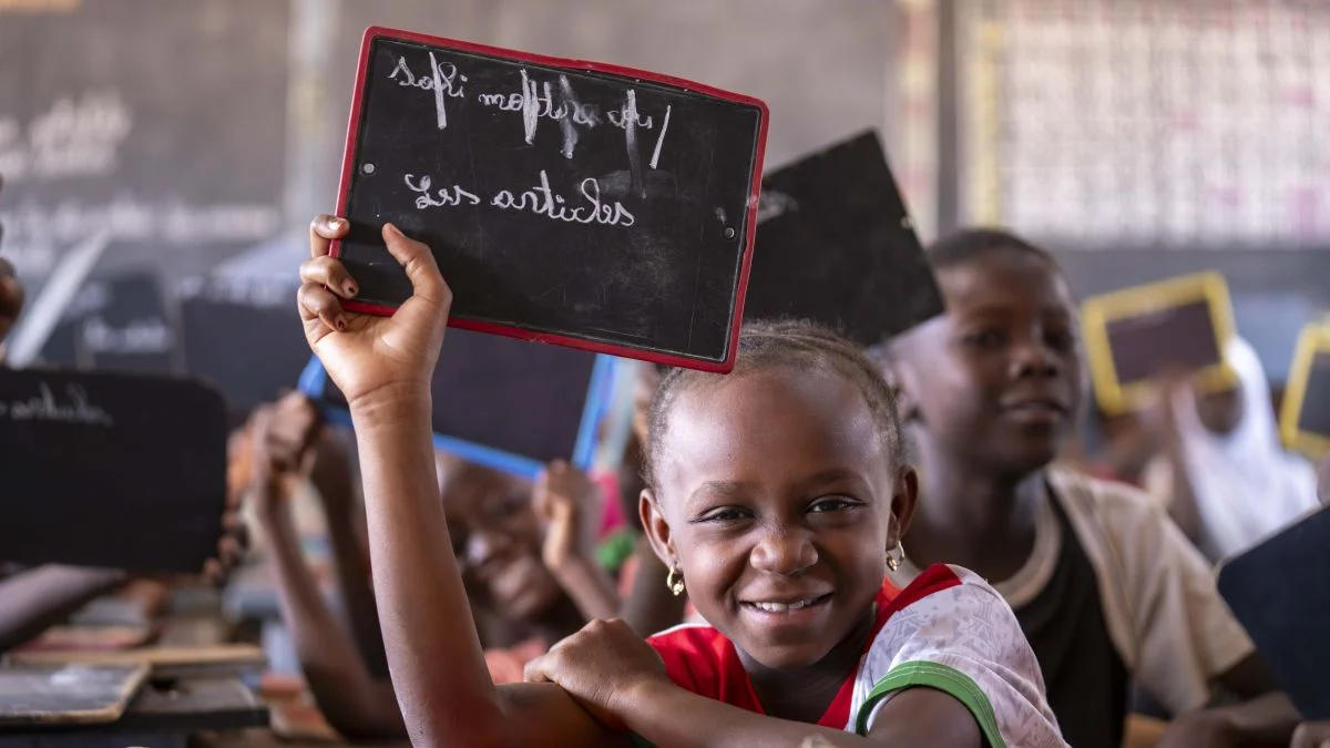Ein Mädchen aus Burkina Faso hält eine Schultafel hoch