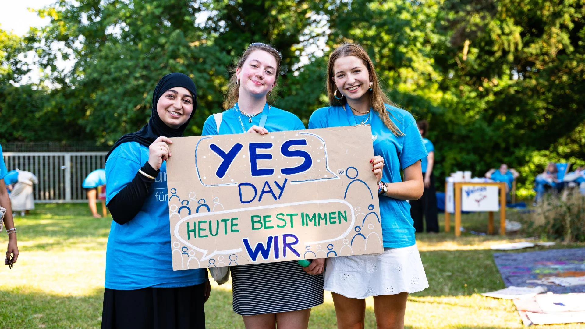 Drei Mädchen halten ein Schild mit dem Text "YES Day Heute bestimmen wir"