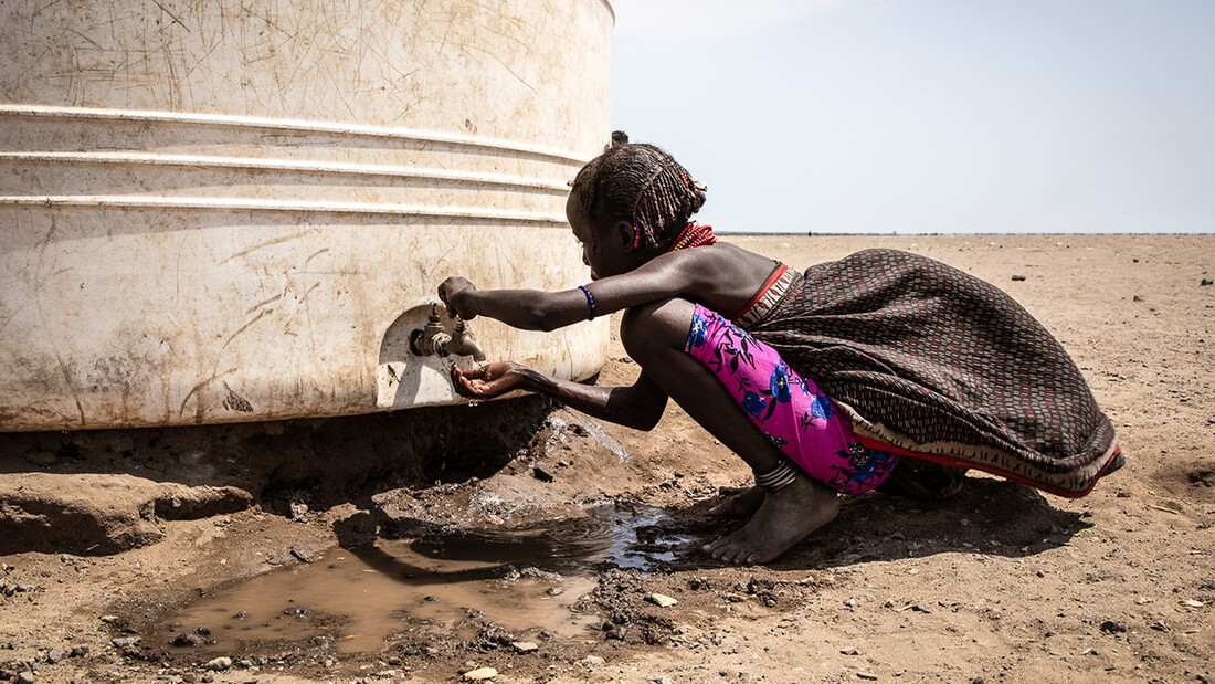 A young girl drinks water from the tap of a water tank.