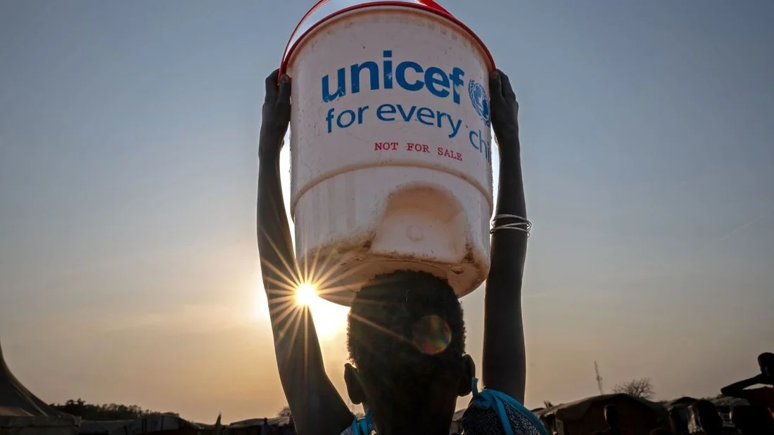 Un bambino porta un secchio d'acqua.