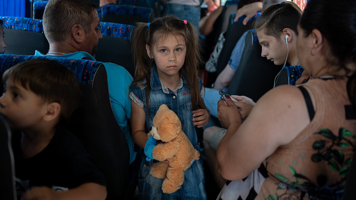 Dmytro, ein Vater von fünf Kindern (links mit dem Rücken), seine Tochter Anya, 7 Jahre alt, und sein Sohn Ernest, 15 Jahre alt (rechts, mit Kopfhörern) sitzen im Evakuierungsbus am Busbahnhof von Cherson.