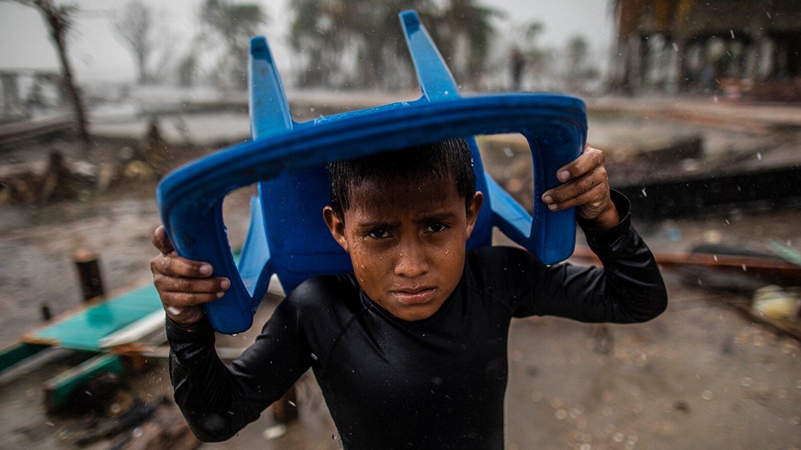 Le 17 novembre 2020 à Bilwi, au Nicaragua, un enfant se protège des fortes pluies avec une chaise en plastique, debout à l'endroit où se trouvait sa maison, après qu'elle ait été détruite par les vents violents, la houle et les pluies provoquées par l'ouragan Iota.