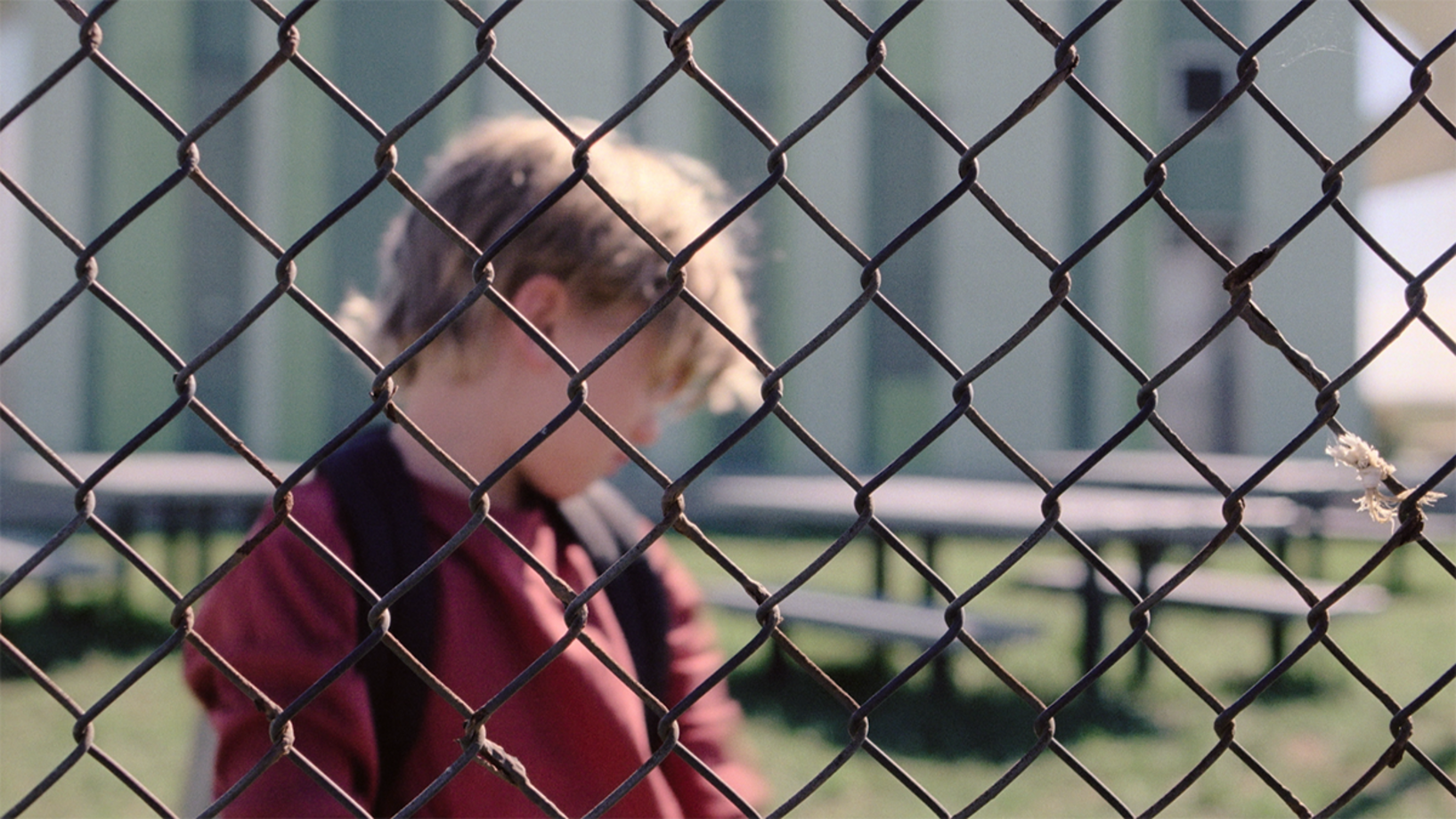 Ein Junge steht hinter einem Zaun.