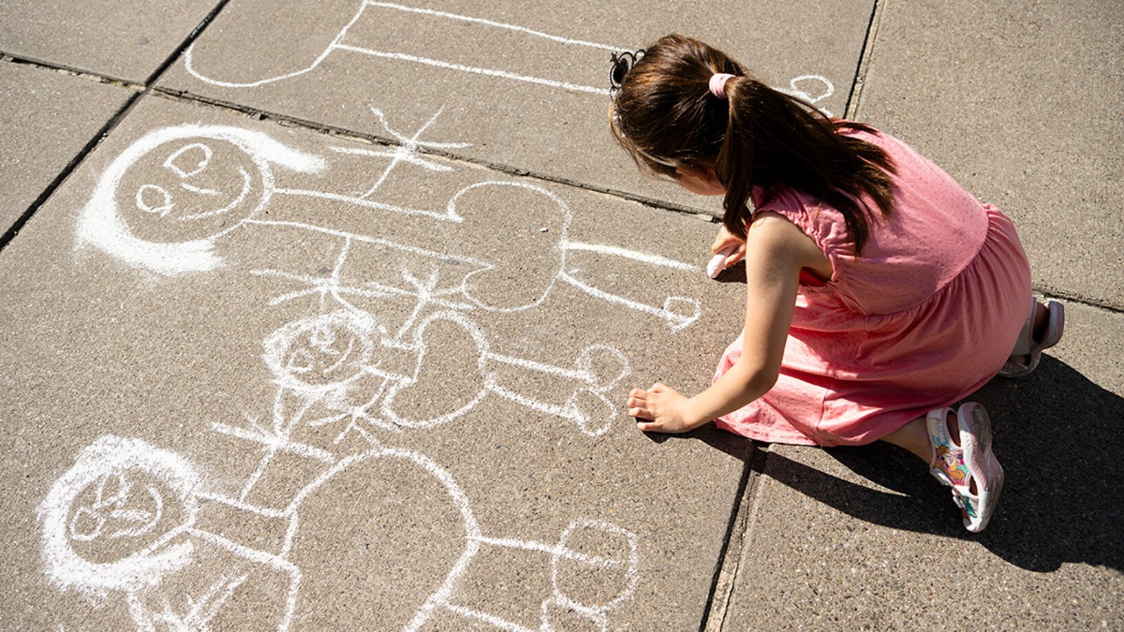 Ein Kind malt mit Kreide Menschen auf den Boden