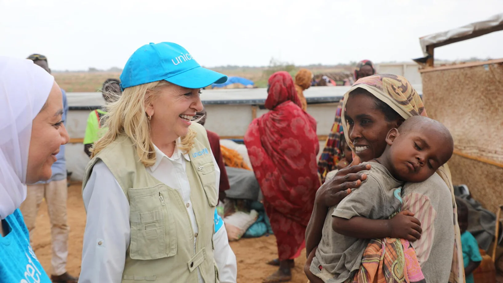 Zwei Mitarbeiterinnen von UNICEF sprechen mit einer Frau, die ihr Kind auf dem Arm trägt