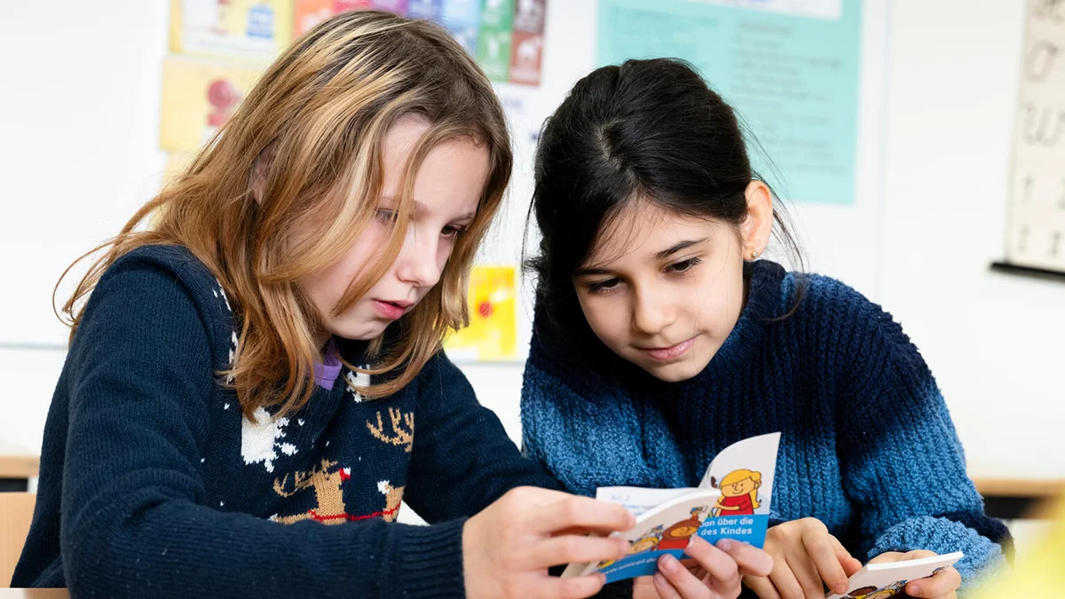 Due ragazze leggono in classe l’opuscolo sulla Convenzione sui diritti dell’infanzia nell’ambito della campagna scolastica «Tu fai parte di noi» 2024.