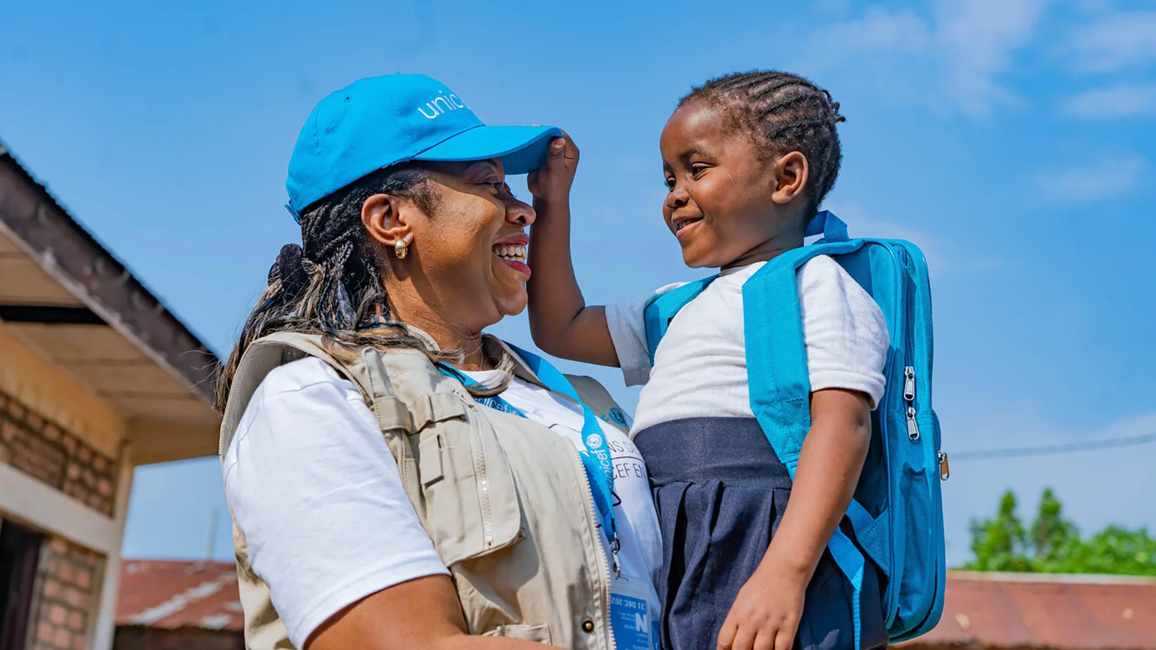 Eine UNICEF-Mitarbeiterin hält ein Mädchen mit UNICEF-Schulranzen im Arm.