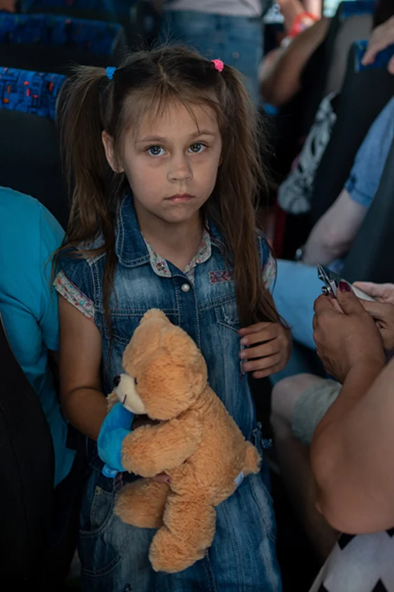 Dmytro, ein Vater von fünf Kindern (links mit dem Rücken), seine Tochter Anya, 7 Jahre alt, und sein Sohn Ernest, 15 Jahre alt (rechts, mit Kopfhörern) sitzen im Evakuierungsbus am Busbahnhof von Cherson.