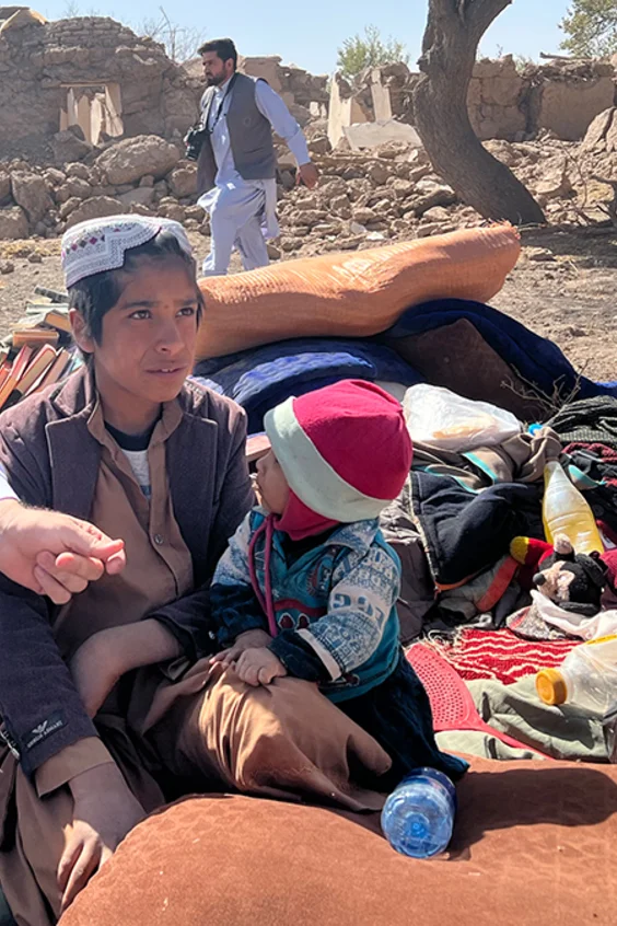 Afghanische Kinder sitzen erschöpft in den wenigen Habseligkeiten, die sie aus ihrem zerstörten Zuhause retten konnten.