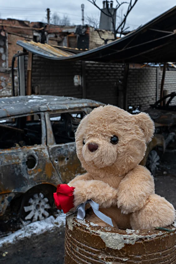 Ein Teddybär und eine rote Rose wurden vor einem völlig zerstörten Haus platziert.