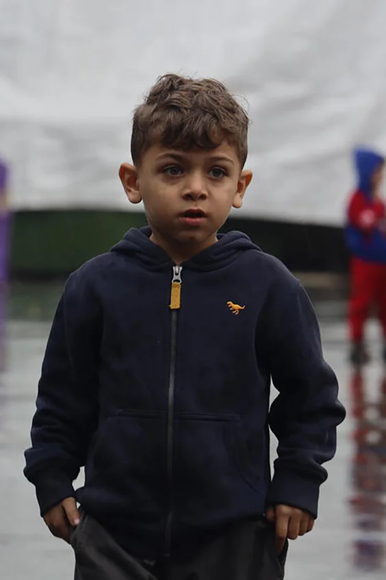 Ein kleiner Junge aus Gaza steht inmitten eines Zeltlagers im Regen.