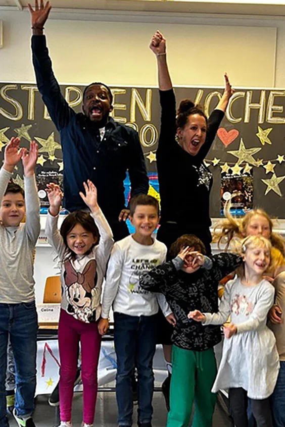 Viele Kinder und Charles Nguela springen in die Luft und jubeln.