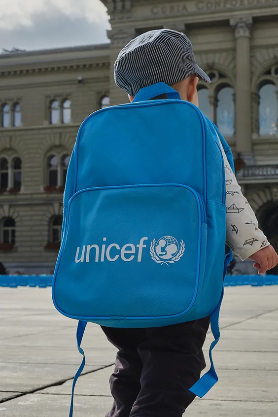 Ein kleiner Junge läuft mit UNICEF Rucksack auf dem Platz vor dem Bundeshaus in Bern.