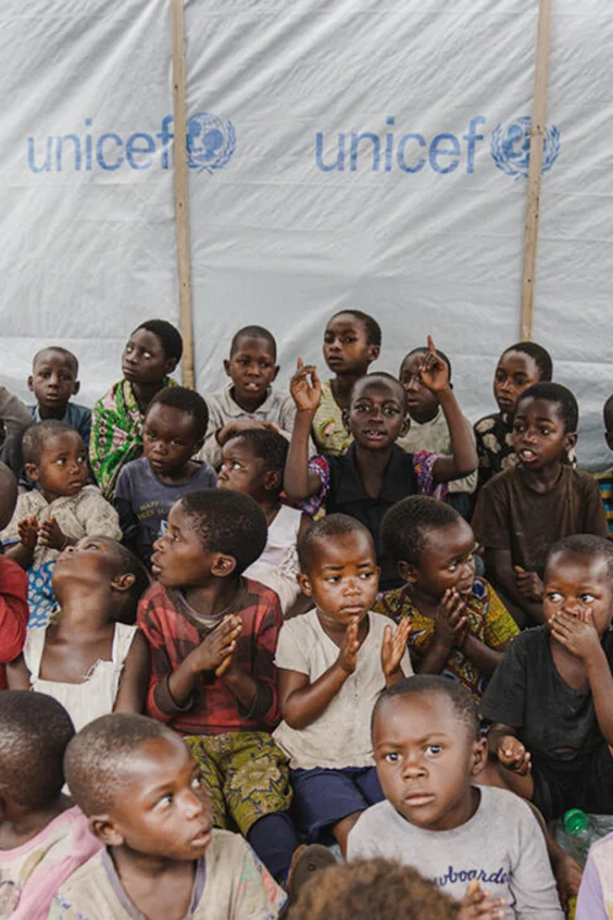 Viele Kinder sitzen auf dem Boden in einem UNICEF-Lernzelt und schauen in die Kamera.