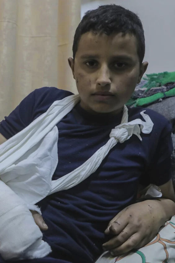 Ein Bub mit einem verletzten Arm sitzt in einem Krankenbett.