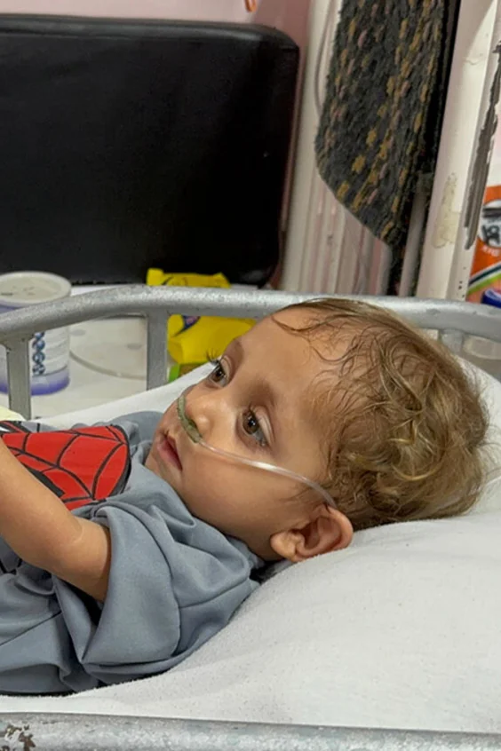 Ein mängelernährtes Kind liegt in einem Krankenhausbett und hält die Hand eines Erwachsenen