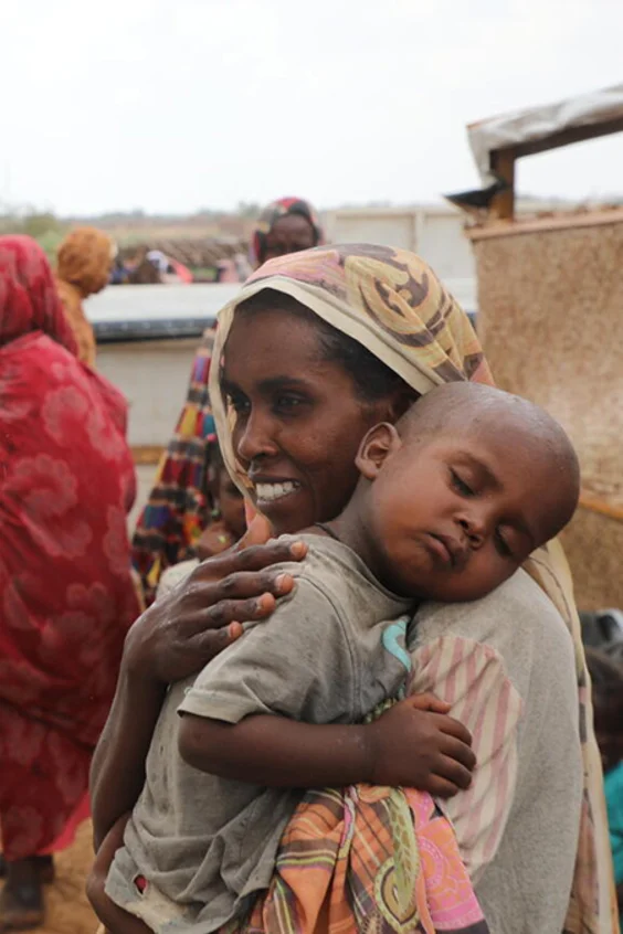 Zwei Mitarbeiterinnen von UNICEF sprechen mit einer Frau, die ihr Kind auf dem Arm trägt
