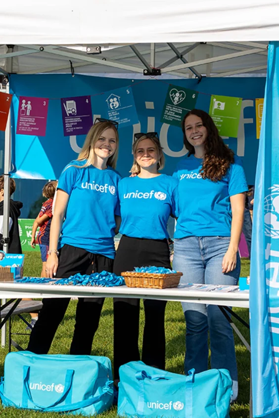 Drei Frauen stehen hinter einem UNICEF Stand und schauen in die Kamera