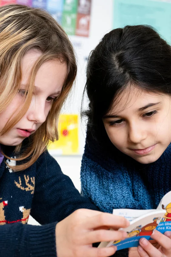 Zwei Mädchen lesen im Unterricht die Broschüre zur Kinderrechtskonvention im Rahmen der Schulaktion «Du gehörst dazu» 2024.